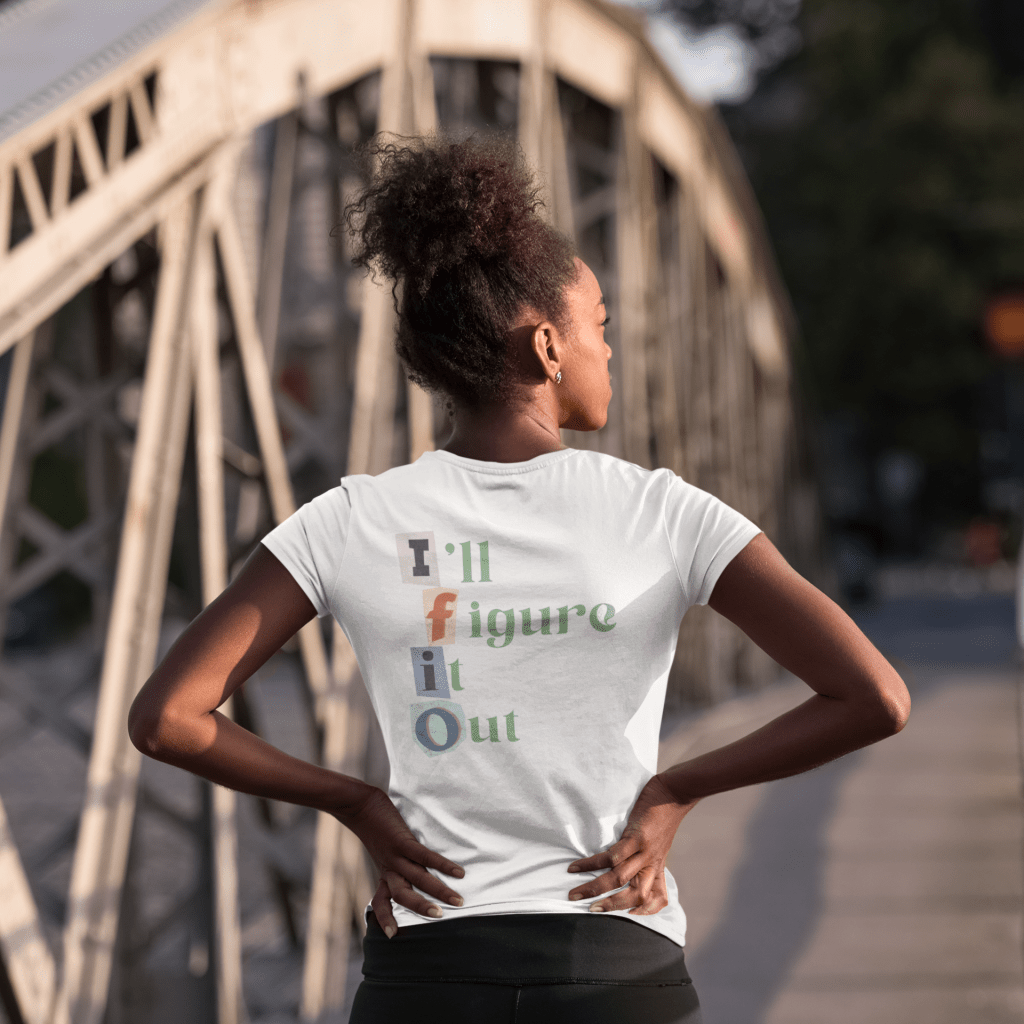 woman showing the back of the IFIO scrapbook lettering t shirt. The back says I'll Figure It Out and the front IFIO with scrapbook style collage lettering.