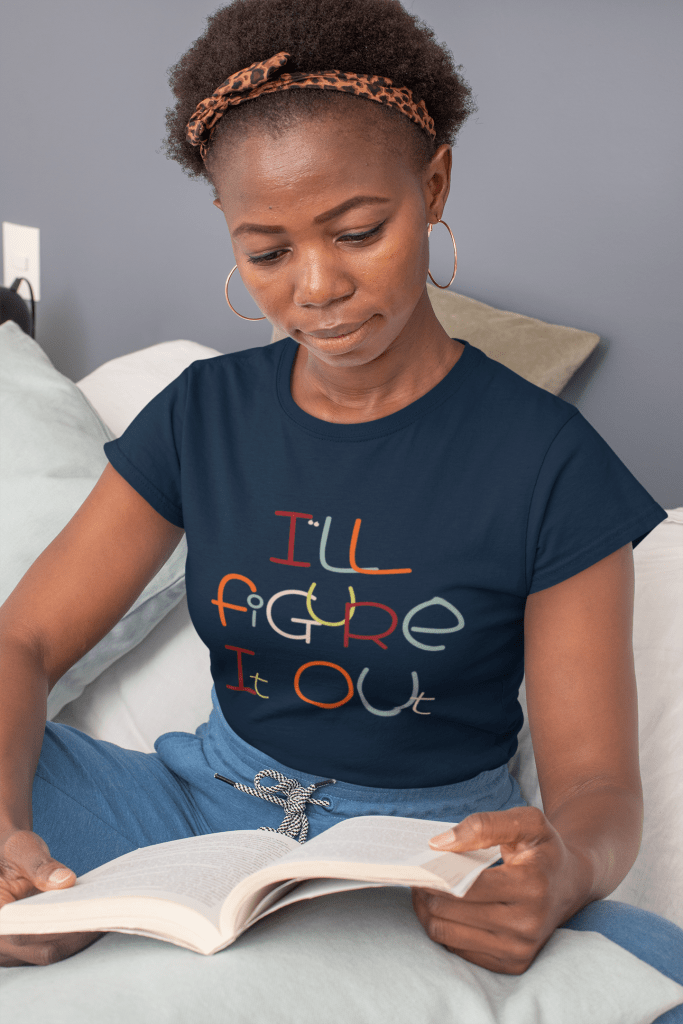 woman looking at a book wearing an I'll Figure It Out t shirt in blue. The design is a whimsical font